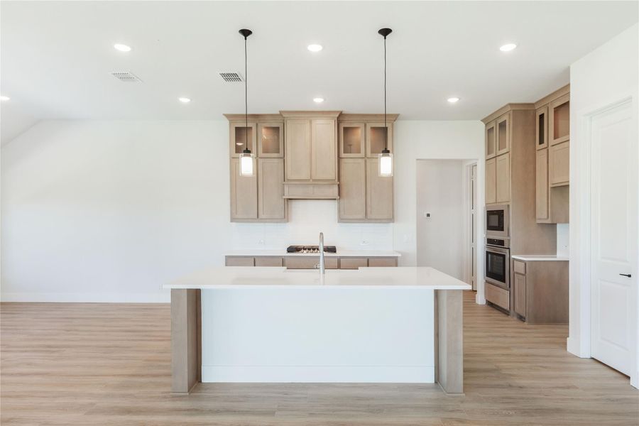 Kitchen with large center island, light wood cabinets, pendant lights, and stainless steel appliances on wood floors