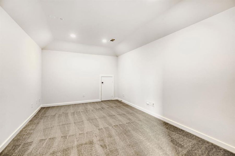 Spacious room featuring vaulted ceilings, recessed lighting, neutral carpet, and a built-in door
