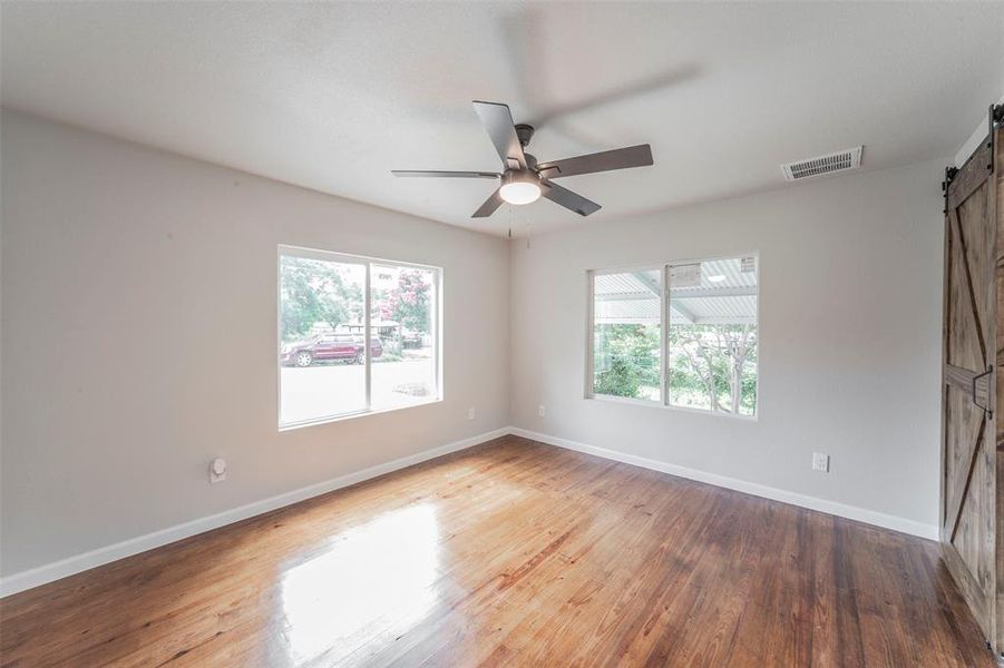 Primary bedroom featuring a wealth of natural light, a barn door, ceiling fan, and hardwood / wood-style flooring