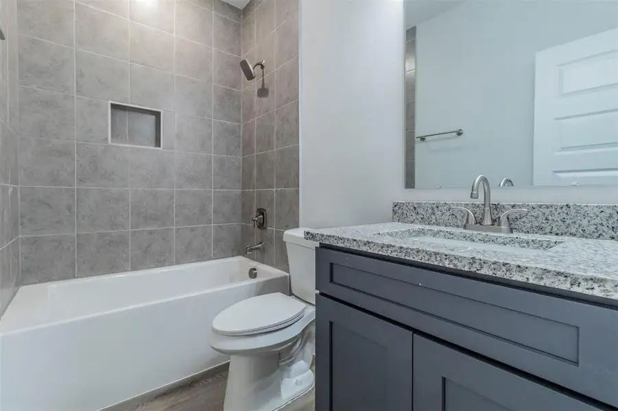 Full bathroom with toilet, tiled shower / bath, wood-type flooring, and vanity