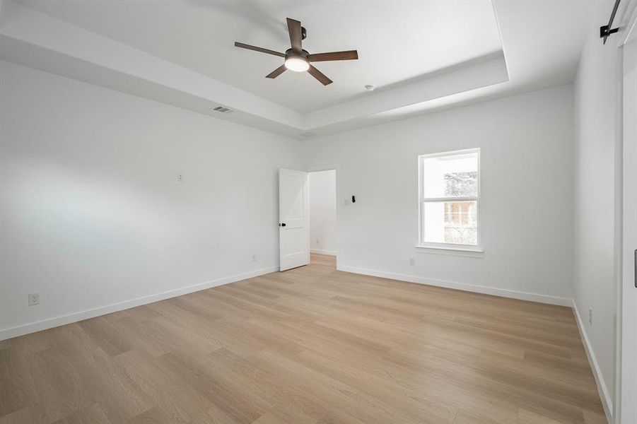 Unfurnished room featuring a raised ceiling, a ceiling fan, and light wood-style floors Unfurnished room featuring a raised ceiling, a ceiling fan, and light wood-style floors