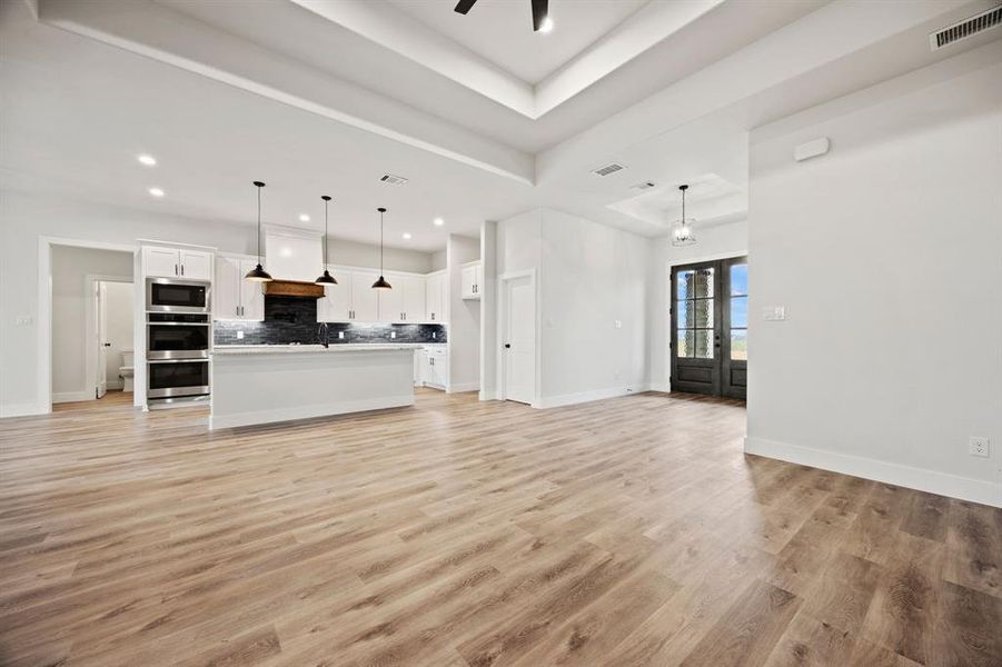 Unfurnished living room with a ceiling fan, baseboards, visible vents, light wood-style floors, and a raised ceiling