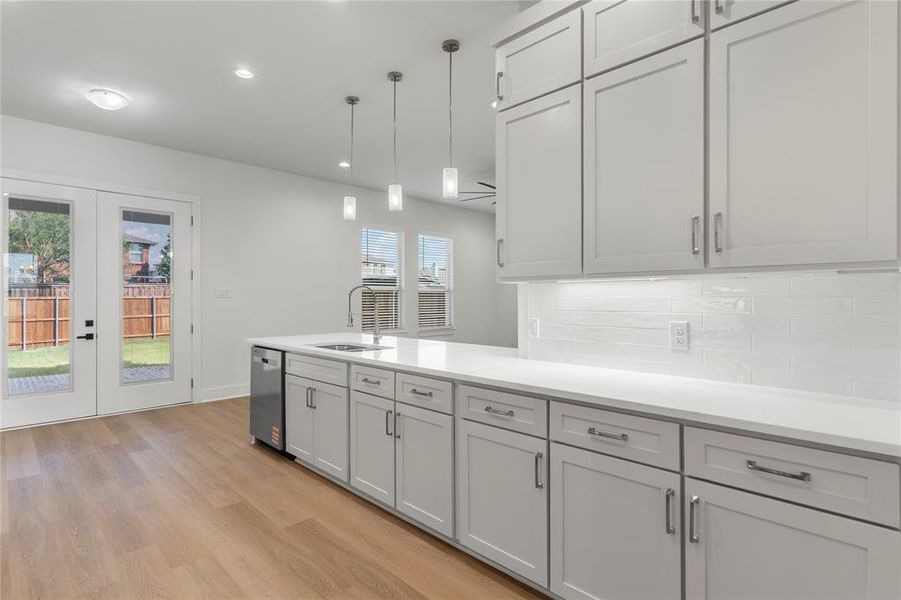 Kitchen with french doors, decorative light fixtures, a peninsula, light wood finished floors, and backsplash Kitchen with french doors, decorative light fixtures, a peninsula, light wood finished floors, and backsplash