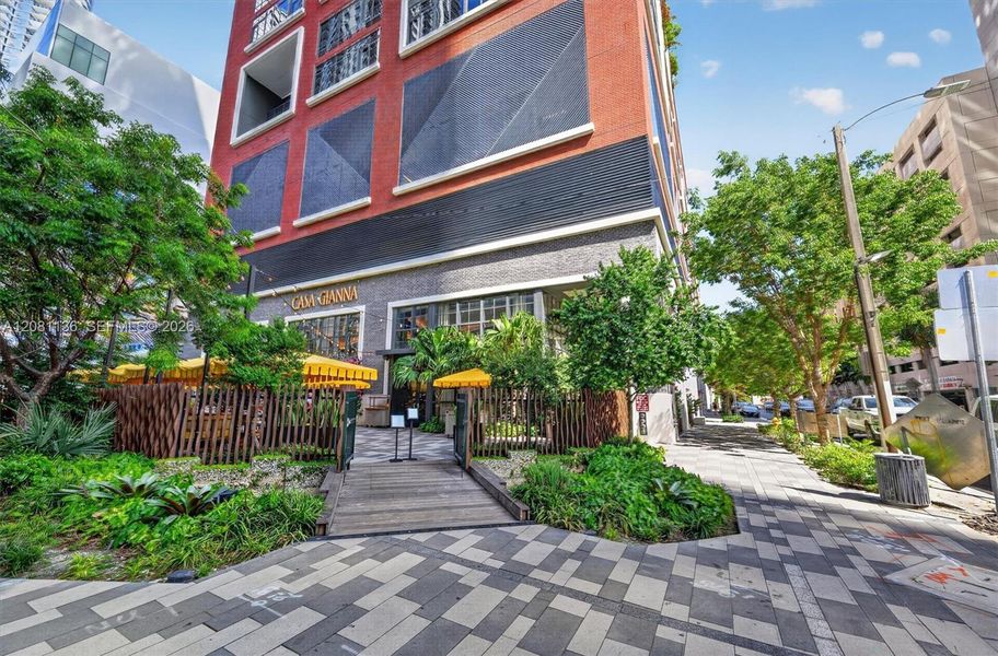 Multi-story brick facade building featuring ground-level commercial frontage, textured stone exterior detailing, and a timber-slat perimeter fence encompassing a paved pedestrian entrance