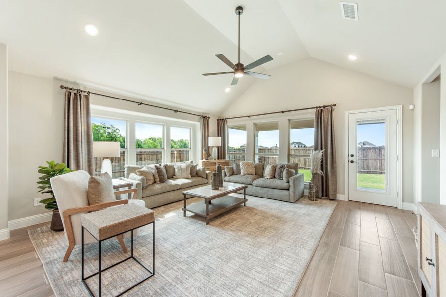 Bright living room with vaulted ceiling, ceiling fan, hardwood floors, and large windows overlooking a backyard.