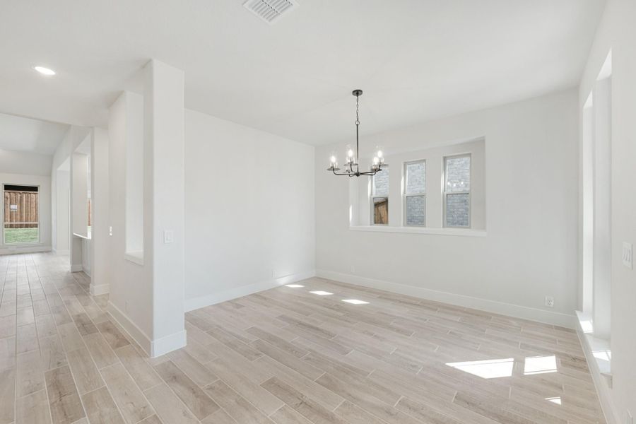 Empty dining room with chandelier, white walls, wood-look tile floors, and two windows