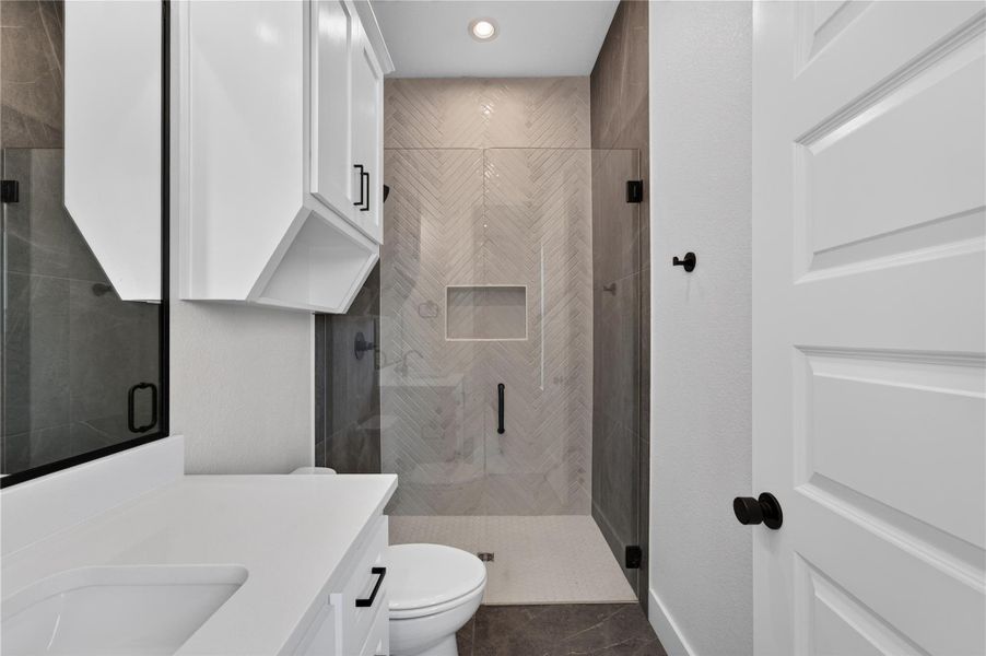 Elegant herringbone tile detailing frames a modern glass-enclosed shower with pristine stone countertops nearby.