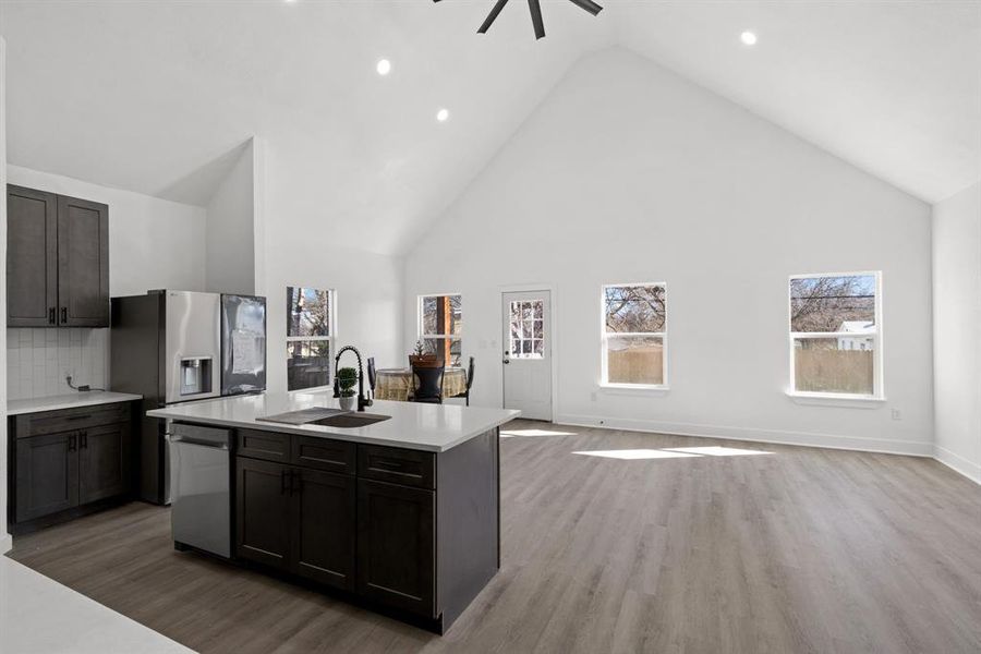 Kitchen featuring sink, high vaulted ceiling, backsplash, a kitchen island with sink, and light wood-type flooring