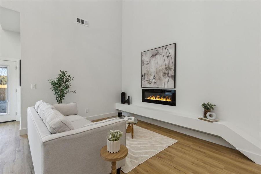 Living room with a fireplace, wood-type flooring, and a towering ceiling