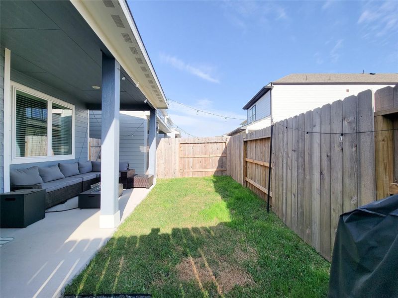 Cozy backyard space with a covered patio featuring outdoor seating. It's bordered by a wooden fence, providing privacy, and includes a grassy area, perfect for relaxation or small gatherings.
