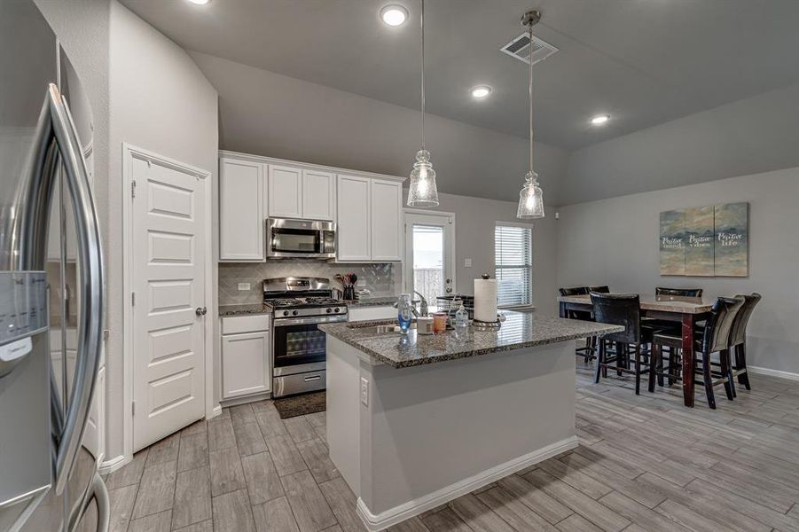 Kitchen with white cabinetry, light hardwood / wood-style floors, stainless steel appliances, and an island with sink