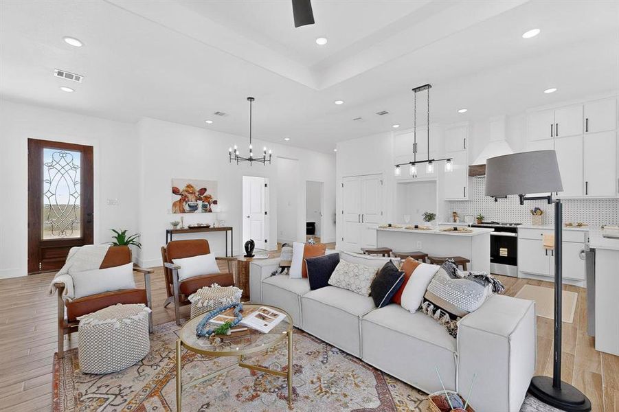 Living room featuring a chandelier, light wood-type flooring, recessed lighting, and a tray ceiling