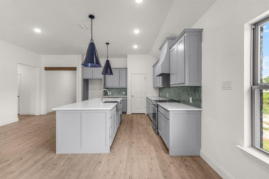 Kitchen with healthy amount of natural light, gray cabinetry, light flooring, stainless steel electric stove, and lofted ceiling