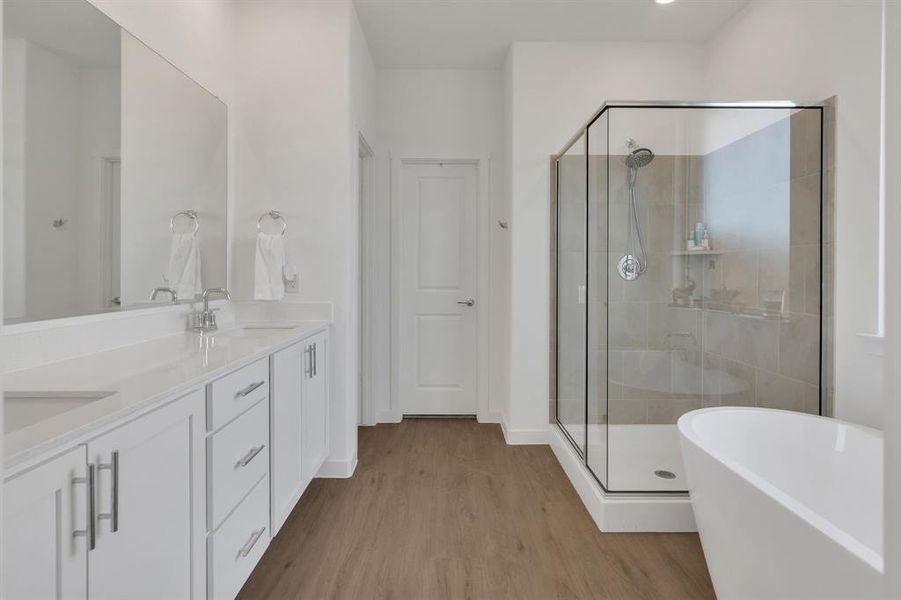 Bathroom featuring a stall shower, a freestanding tub, double vanity, and light wood finished floors