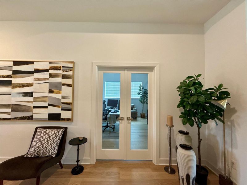 Elegant interior featuring glass double doors leading to home office complemented by modern decor and a large abstract painting.