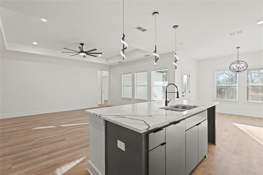 Kitchen with a tray ceiling, a center island with sink, visible vents, light wood-style flooring, and a sink