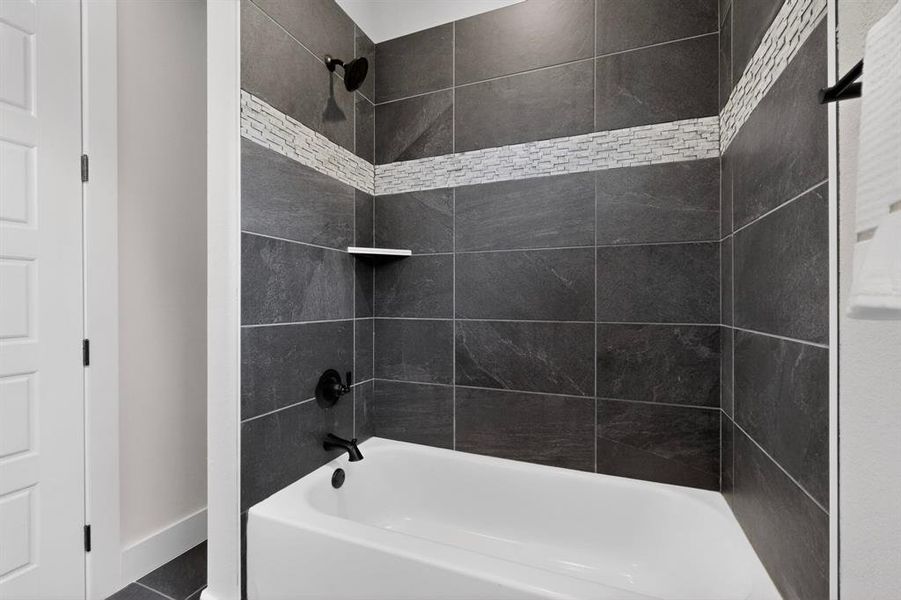 Shower-over-tub combination featuring dark gray wall tiling with a decorative mosaic band, matte black fixtures, and a white integrated tub