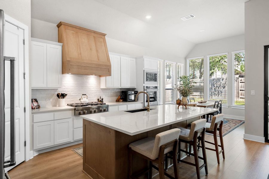 Well-appointed kitchen featuring white shaker cabinetry and a natural wood-finish range hood