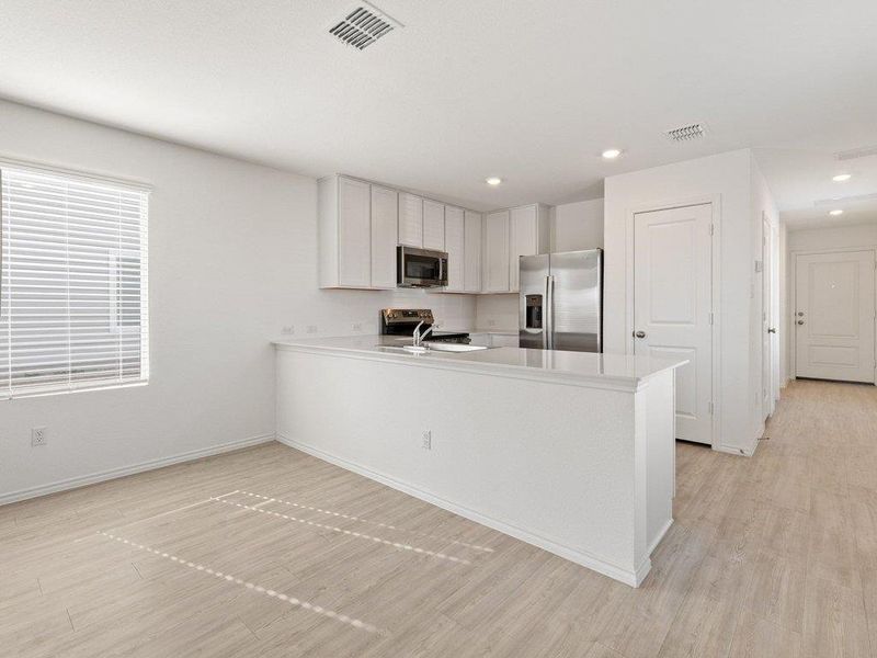 Kitchen with light countertops, white cabinets, stainless steel appliances, a peninsula, and light wood-style floors