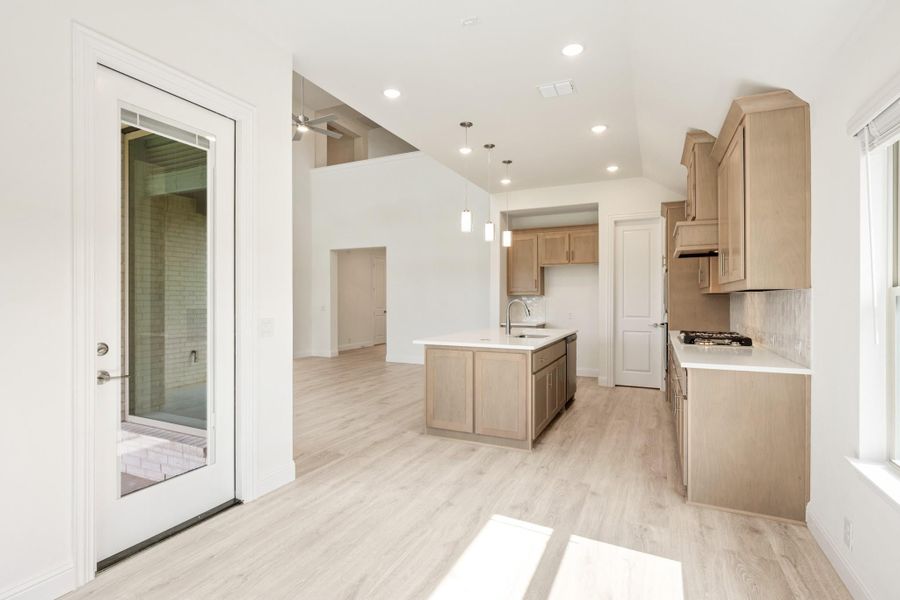 Open kitchen with light wood cabinets, center island, pendant lights, and light hardwood floors