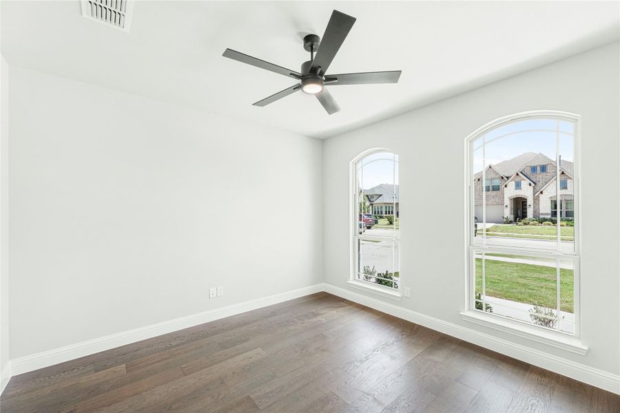 Empty room with dark hardwood floors, ceiling fan, and two arched windows overlooking a neighborhood street. Empty room with dark hardwood floors, ceiling fan, and two arched windows overlooking a neighborhood street.