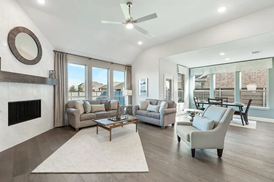 Open living room with vaulted ceiling, tile fireplace, hardwood floors, and ceiling fan