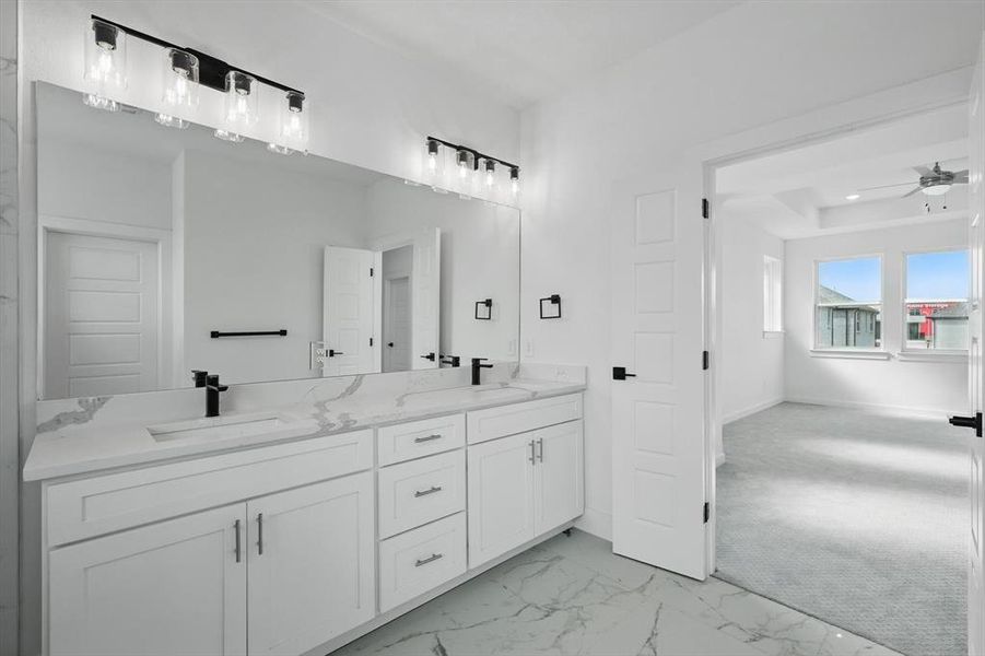 Full bathroom with double vanity, a ceiling fan, marble look tiles, and baseboards