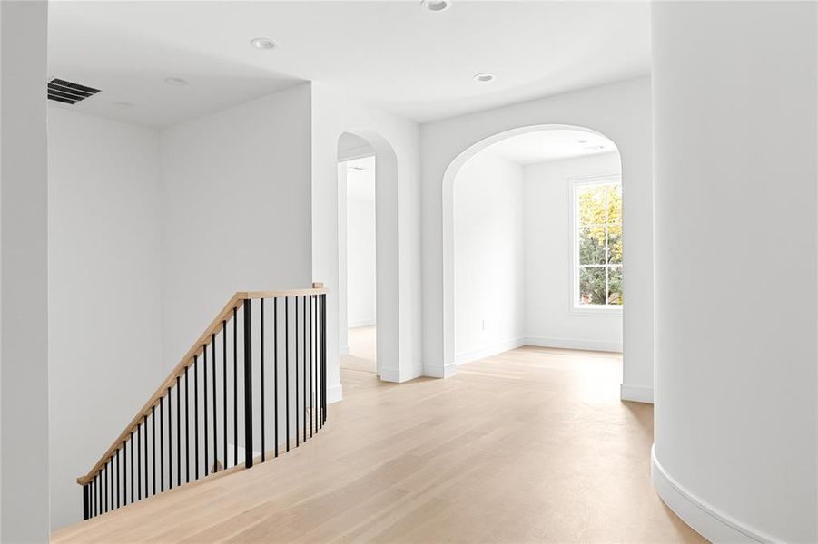Hall with arched walkways, light wood-style floors, and recessed lighting