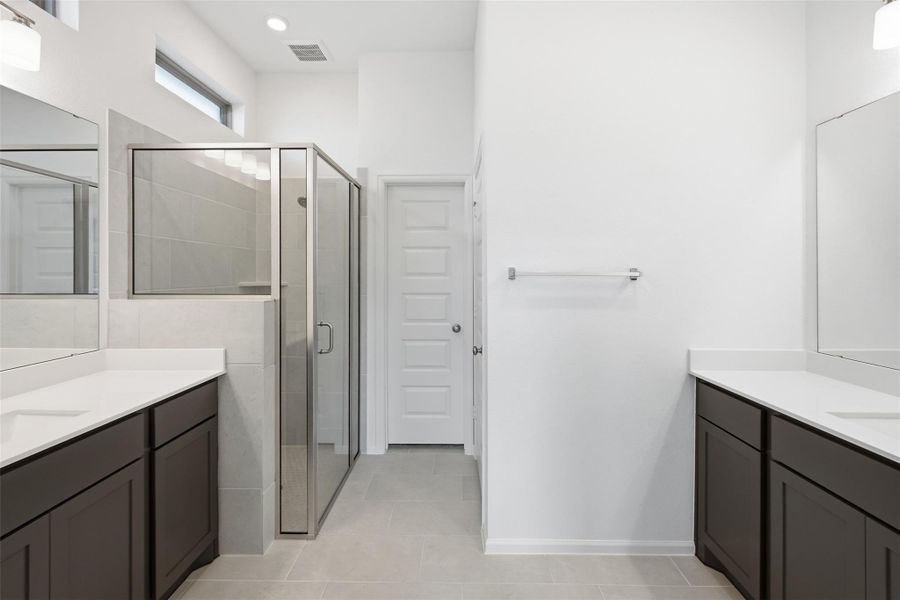 Bright and modern bathroom with dual vanities, sleek dark cabinetry, and a spacious glass-enclosed shower, offering a clean and elegant design.
