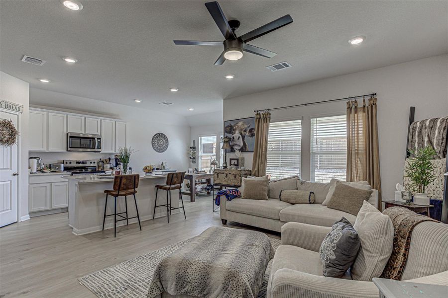 Living area with a ceiling fan, light wood finished floors, recessed lighting, and a textured ceiling