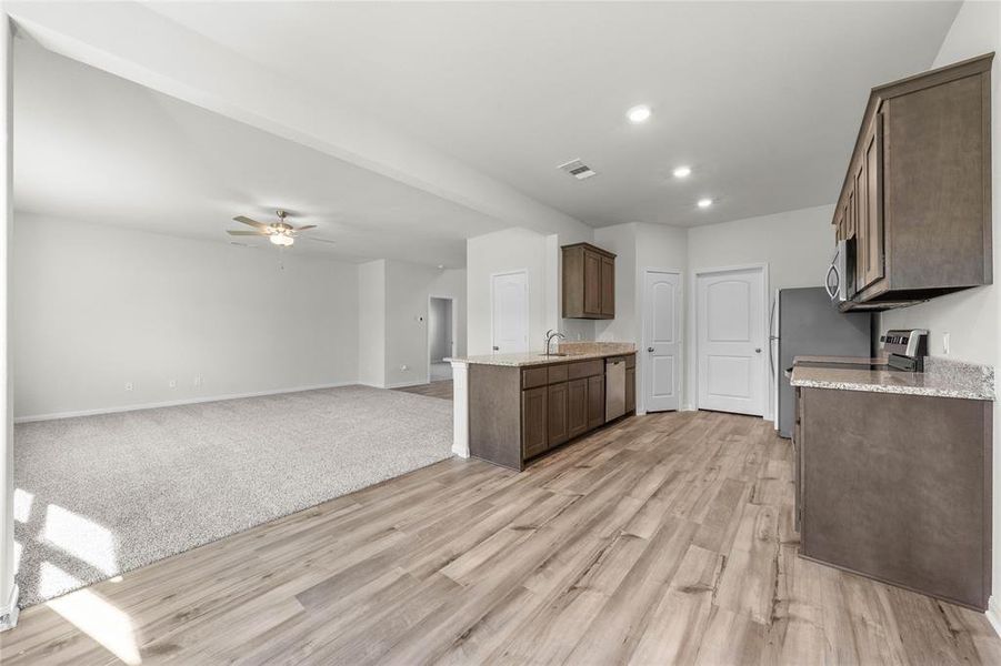 Kitchen with light wood finished floors, ceiling fan, appliances with stainless steel finishes, open floor plan, and a sink