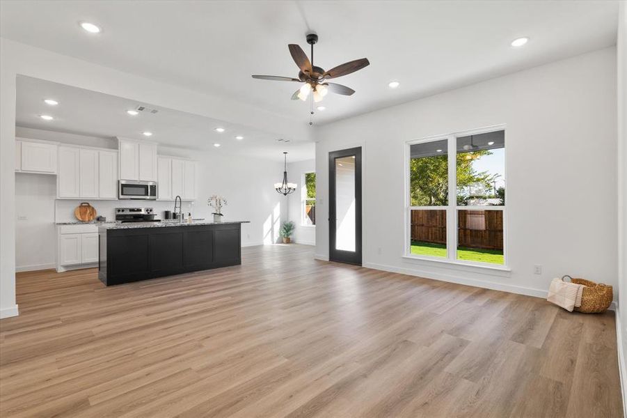 Kitchen with an island with sink, white cabinetry, hanging light fixtures, light hardwood / wood-style flooring, and appliances with stainless steel finishes