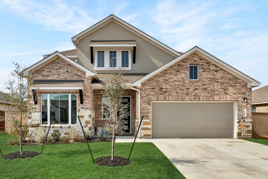 View of front of house featuring brick siding, and stucco siding, and a tandem garage.