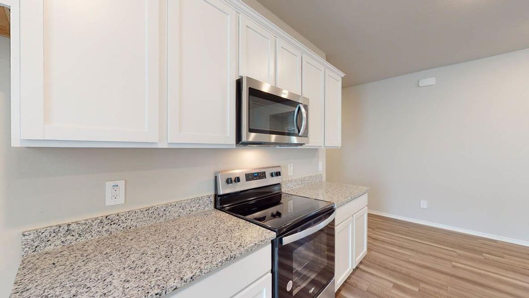 Kitchen with appliances with stainless steel finishes, white cabinetry, light stone counters, and light wood-style floors