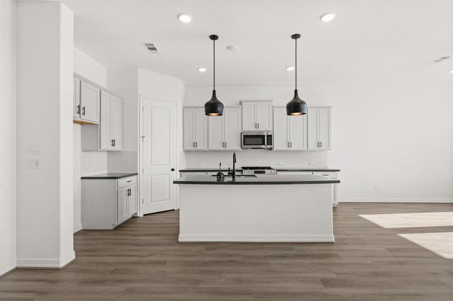 This light and bright kitchen features a large quartz island, white cabinets, a large sink overlooking your family room, recessed lighting, and beautiful backsplash.