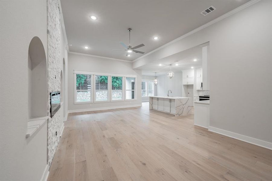 Unfurnished living room featuring crown molding, light wood-type flooring, ceiling fan, a chandelier, and recessed lighting