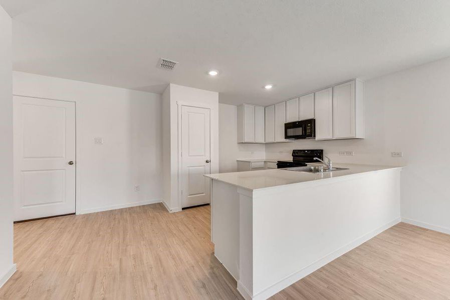 Kitchen featuring black appliances, a peninsula, light countertops, and white cabinetry