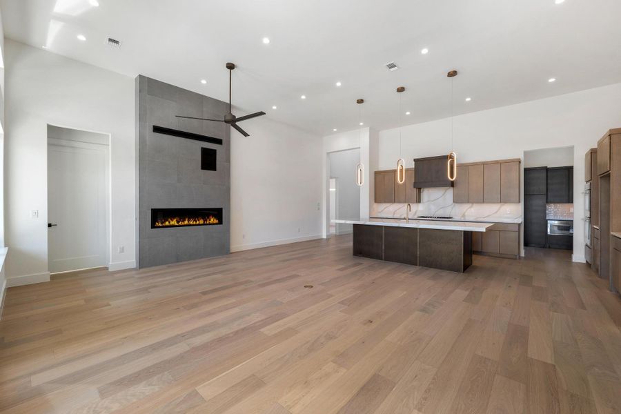 Kitchen with open floor plan, a large island with sink, modern cabinets, backsplash, and a fireplace