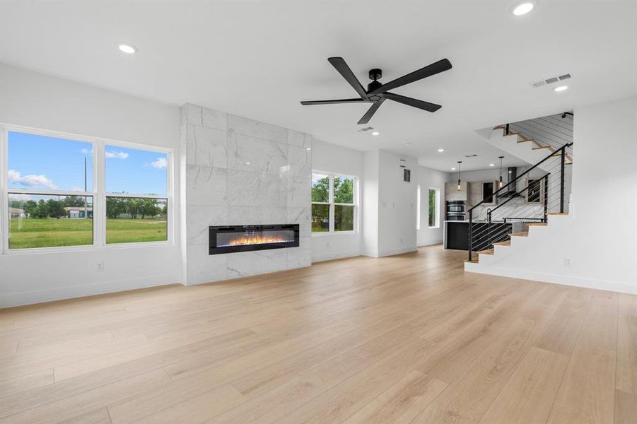 Unfurnished living room featuring a tiled fireplace, visible vents, baseboards, and stairs