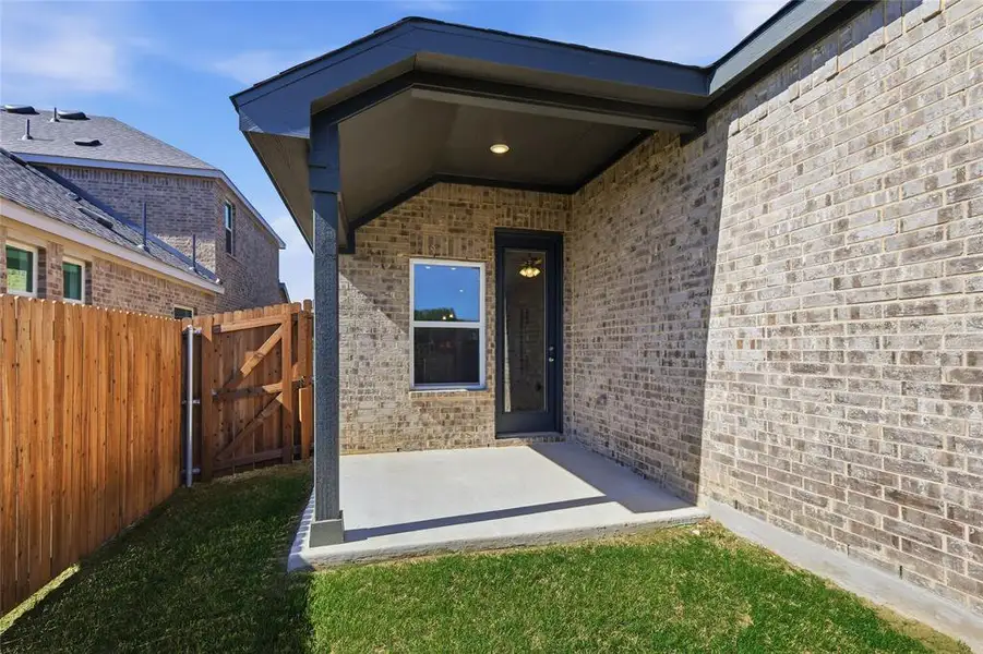 Doorway to property with brick siding, a patio area, a gate, and a yard Doorway to property with brick siding, a patio area, a gate, and a yard