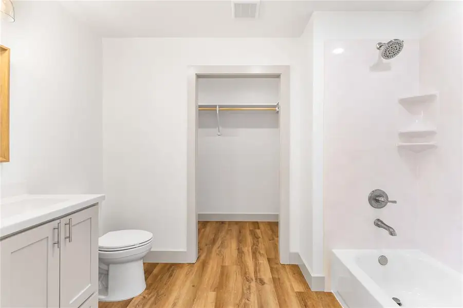 Full bathroom featuring wood finished floors, washtub / shower combination, toilet, vanity, and a walk in closet Full bathroom featuring wood finished floors, washtub / shower combination, toilet, vanity, and a walk in closet