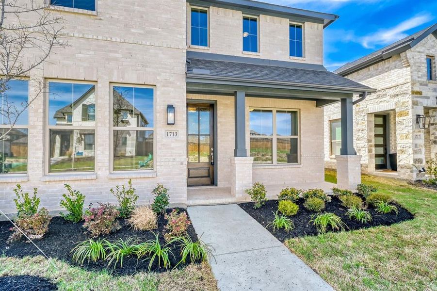Doorway to property with a porch, brick siding, and a shingled roof