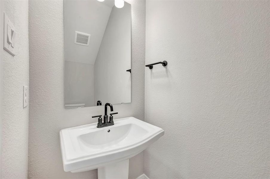Bathroom featuring a textured wall and vaulted ceiling