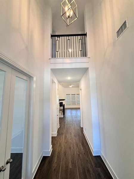 Hallway with a towering ceiling, dark hardwood / wood-style flooring, and a chandelier