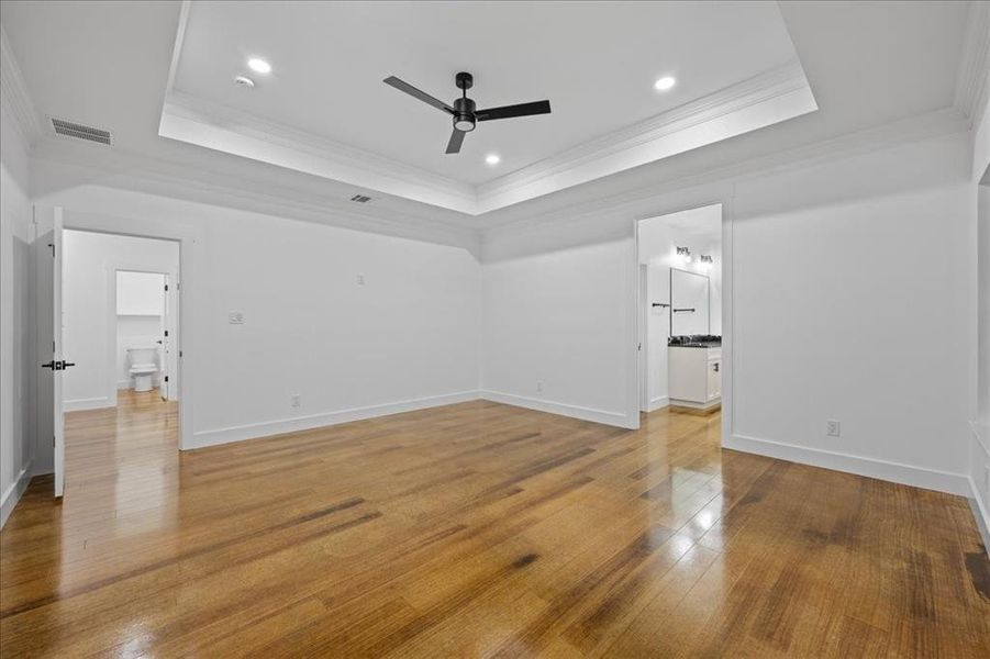 Retreat to your own sanctuary featuring crown molding, recessed lighting, wood-style flooring, ceiling fan, and a tray ceiling