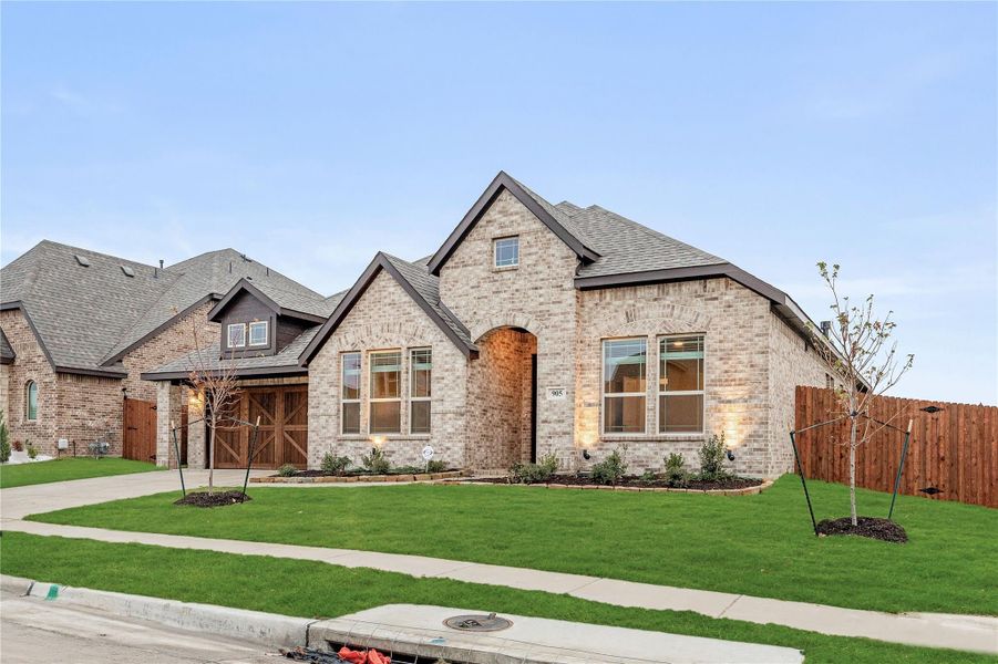 Single-story brick home with arched entry, wood garage door, and manicured front lawn