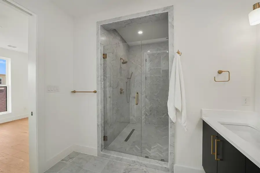 Glass-enclosed shower with a rainfall showerhead, marble-style wall tiles in a herringbone pattern, coordinating marble-style floor tiles, and a linear drain Glass-enclosed shower with a rainfall showerhead, marble-style wall tiles in a herringbone pattern, coordinating marble-style floor tiles, and a linear drain