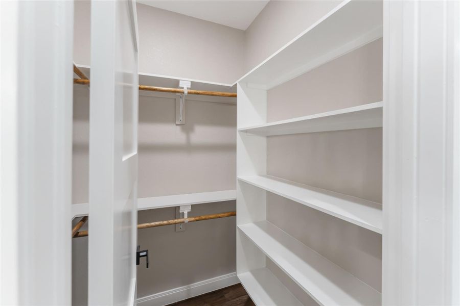 This photo shows a walk-in closet with white shelving on the right and wooden hanging rods on the left. The space is well-organized, providing ample storage for clothes and other items.