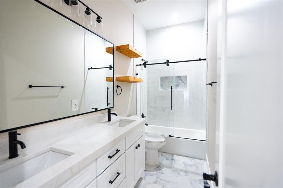 Full bath with bath / shower combo with glass door, double vanity, and light marble finish flooring