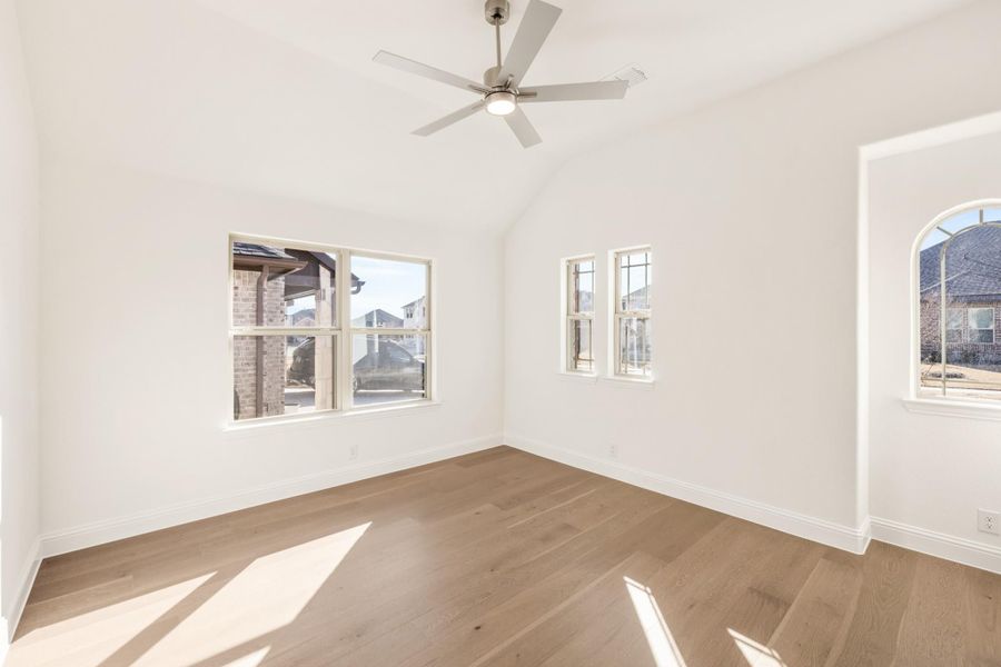 Empty room with vaulted ceiling, ceiling fan, hardwood floors, and multiple windows with natural light Empty room with vaulted ceiling, ceiling fan, hardwood floors, and multiple windows with natural light